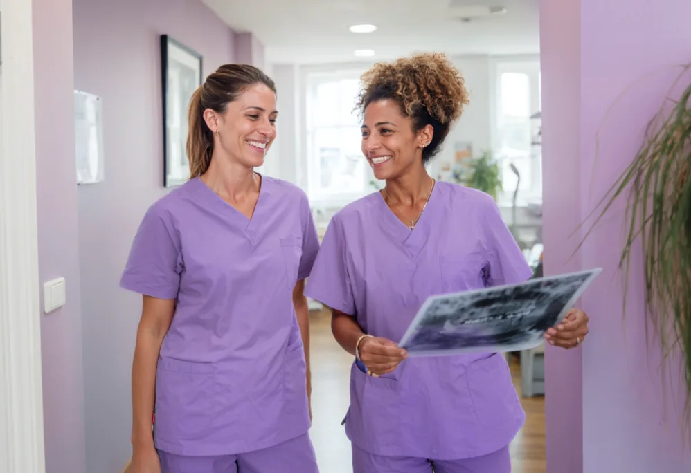 Two dentists in lilac scrubs chatting in the clinic