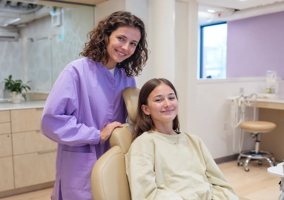 A dentist smiling with a young patient in the dental chair